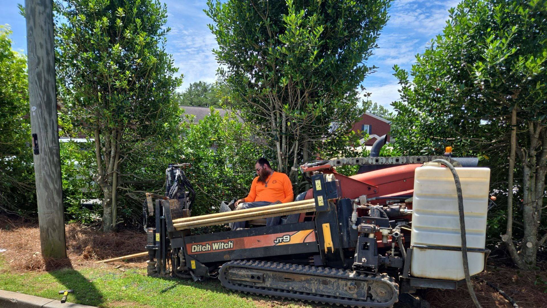 A DUGS operator running a Ditch Witch JT9 directional drill on a residential verge, boring underground with the grass left intact